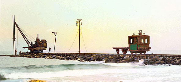 Basaltblokkenvervoer op golfbreker/strandhoofd 11 bij Monster-Ter Heijde. Ex-RTM normaalspoorloc (van de RTM-lijn Rotterdam-Schiedam?) met platte wagen. 13 augustusus 1910. De oorspronkelijke foto heb ik voor contrast, scherpte en kleur op AI losgelaten, dus het is wel een beetje geschiedsvervalsing.